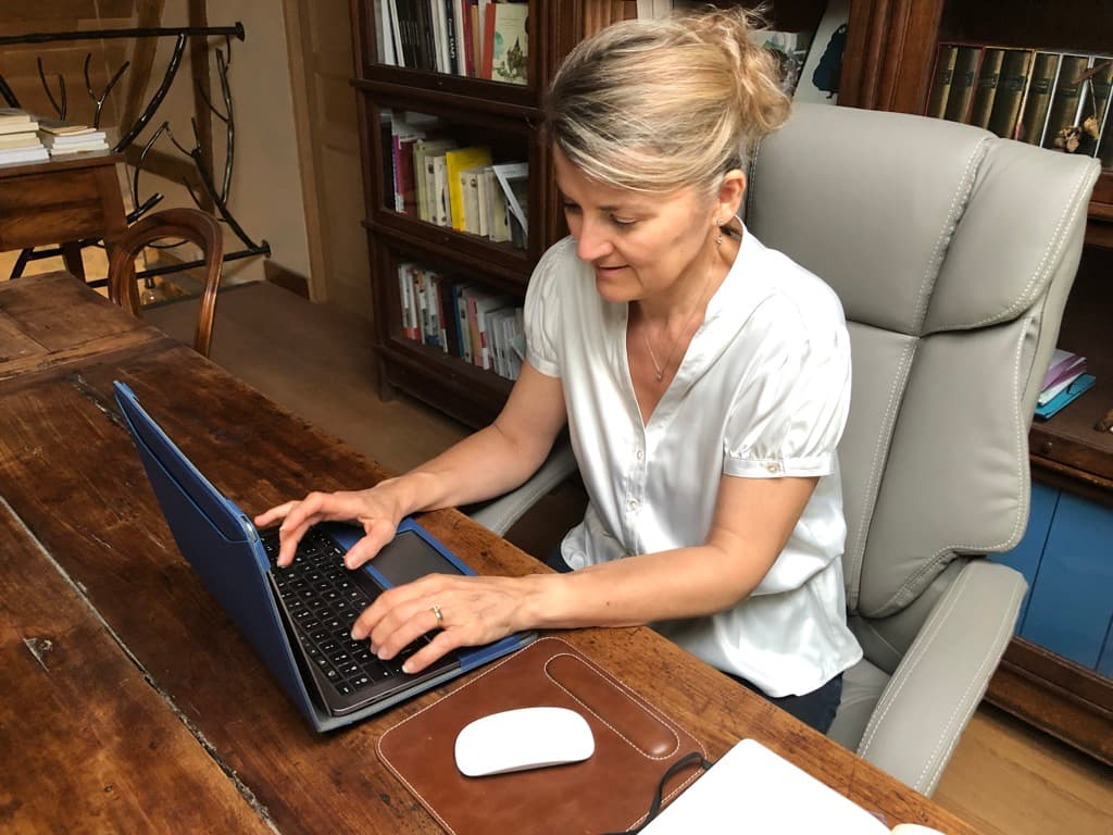Domitille Raillon rédige à l'ordinateur dans son bureau, bibliothèque en arrière-plan